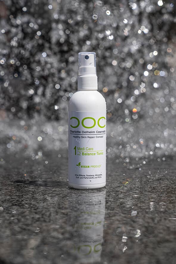 COC Kosmetikprodukt steht auf einem grauen Stein. In der Luft gibt es viele Wassertropfen, die in dem Licht schimmern.